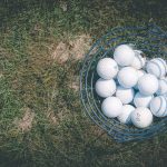 A basket full of golf balls resting on a sunlit lawn, perfect for sports and leisure themes.