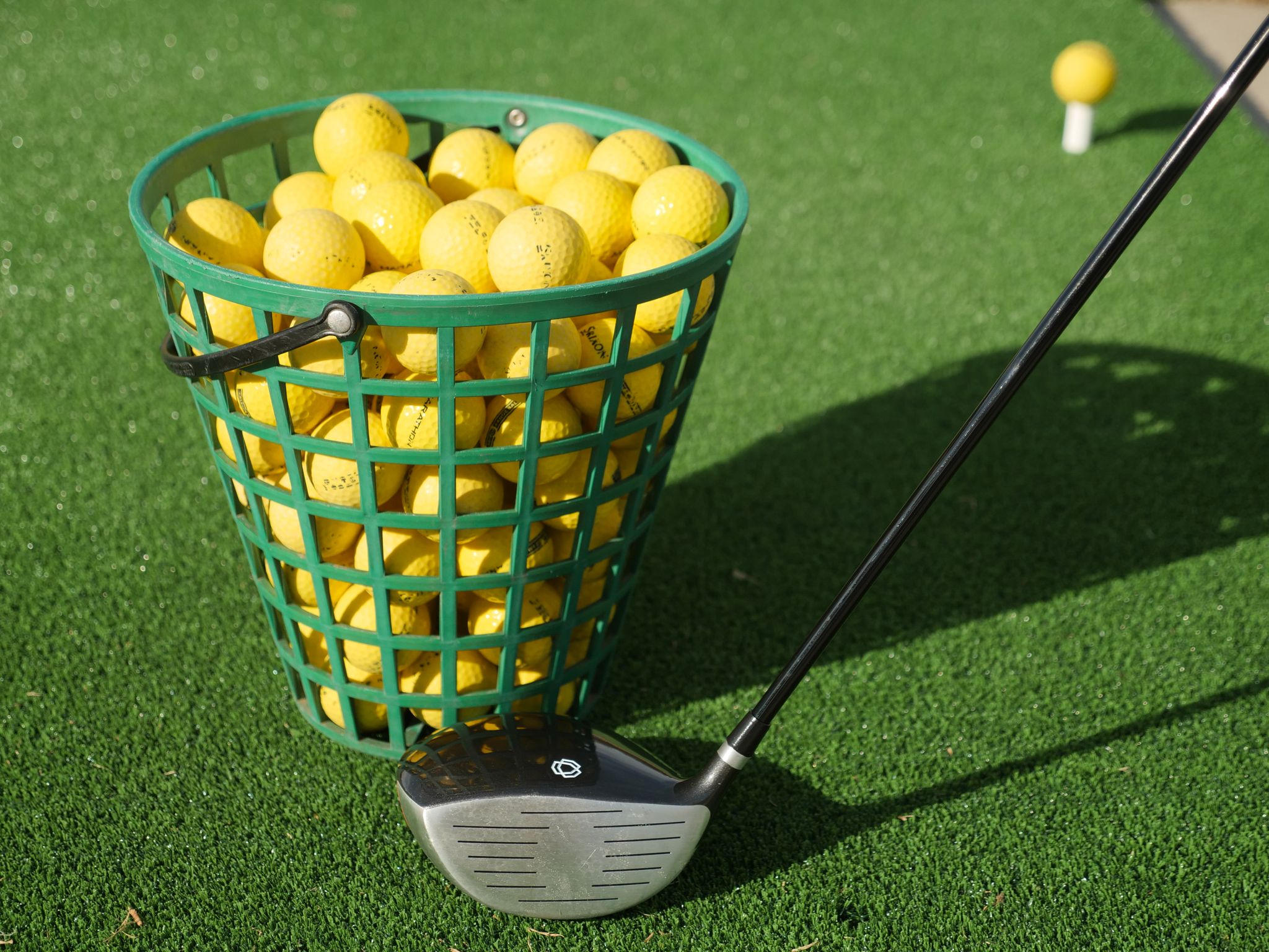 A close-up of a basket full of yellow golf balls with a golf club on green turf, ideal for sports imagery.