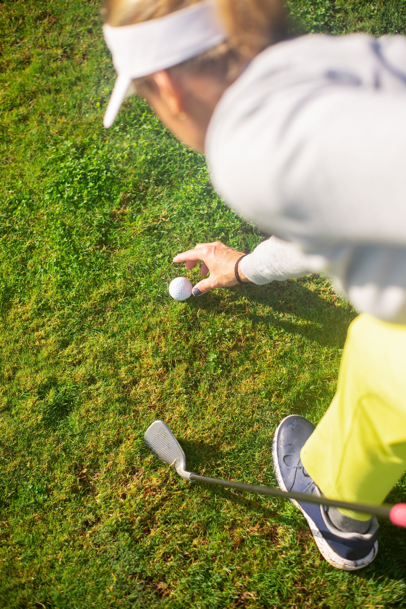 An unrecognizable golfer prepares to play a shot on the lush green grass of a golf course.