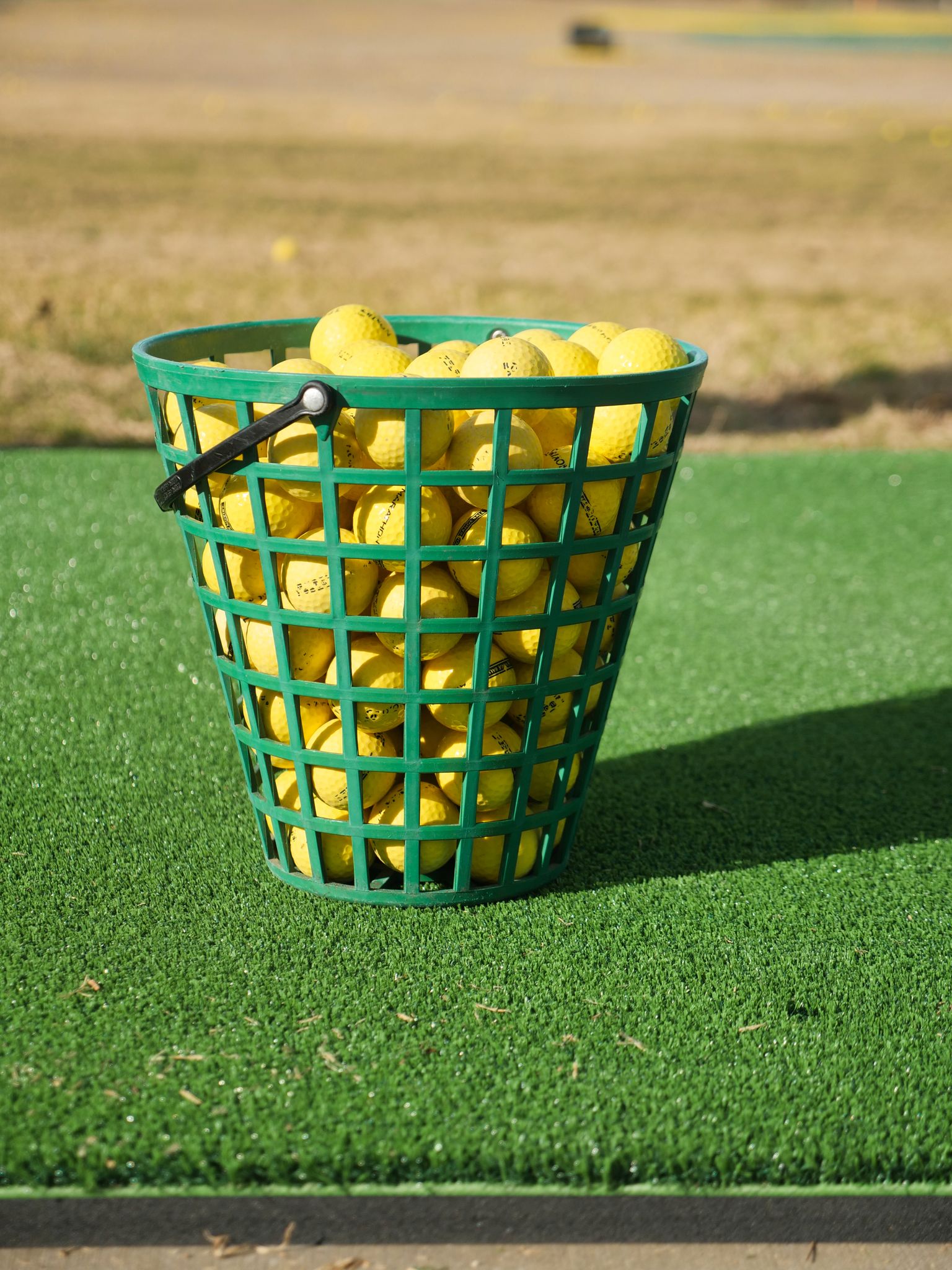 Basket filled with yellow golf balls on artificial turf outdoors.