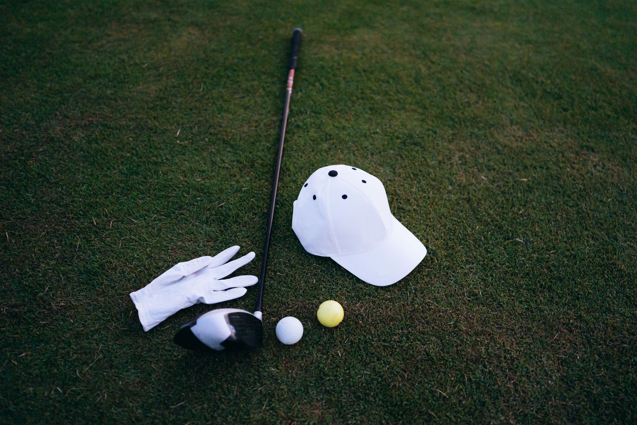 Close-up of golf club, balls, glove, and cap placed on green grass, perfect for a golf day.
