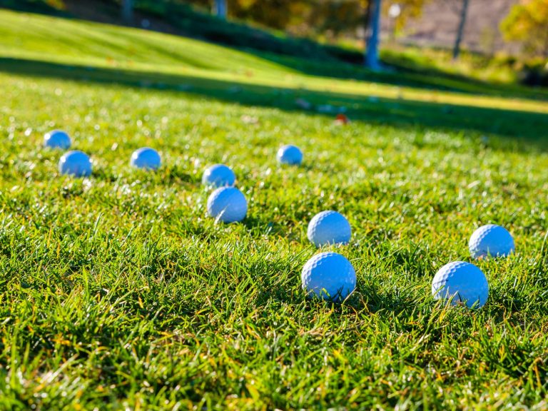 Golf balls scattered on a vibrant green fairway under sunny skies.