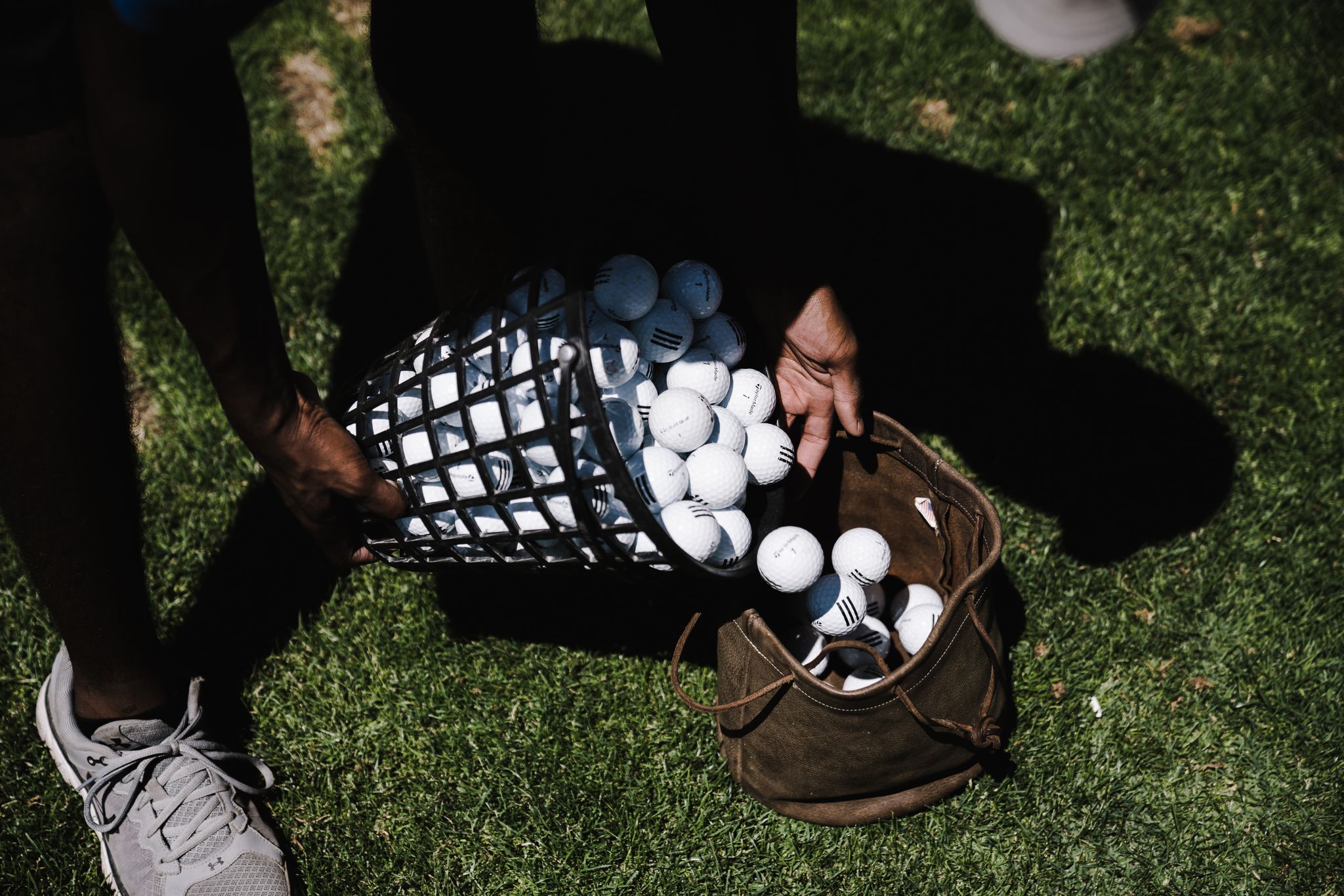 Person transferring golf balls into a bag on a grassy field, outdoors.